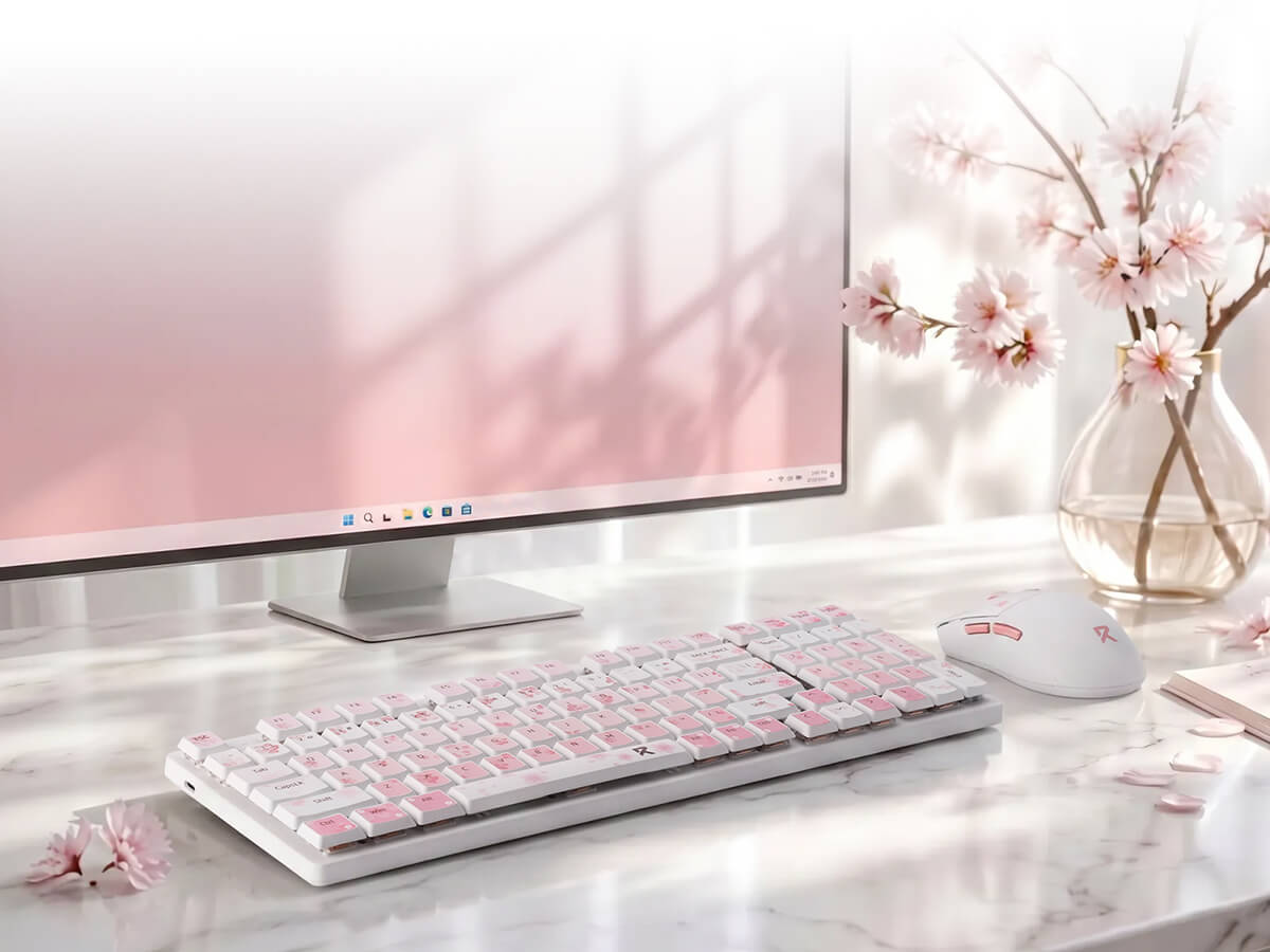 A white and pink wireless keyboard and matching mouse on a marble desk, styled with a computer monitor, cherry blossom flowers in a glass vase, and soft window shadows.