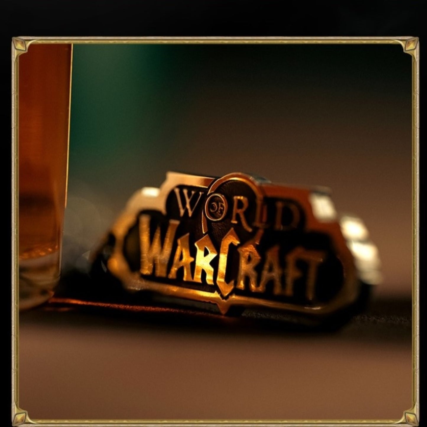 Set within a gold-accented frame, a metallic "WORLD OF WARCRAFT" emblem (shimmering in warm tones) rests beside a blurred glass of amber liquid, against a softly lit, gradient background.