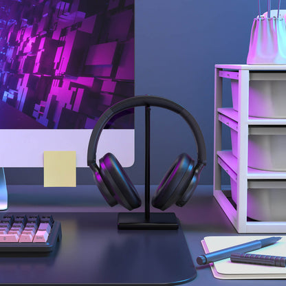 Black headphones on a stand in front of a computer monitor with a purple and blue color scheme.