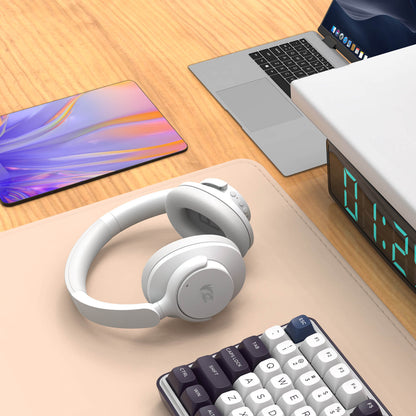 White headphones on a desk with a laptop, tablet, and digital clock in the background.