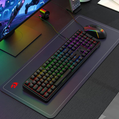 A Redragon RGB mechanical keyboard and gaming mouse are displayed on a branded desk mat in a modern gaming setup, with a monitor and webcam in the background.