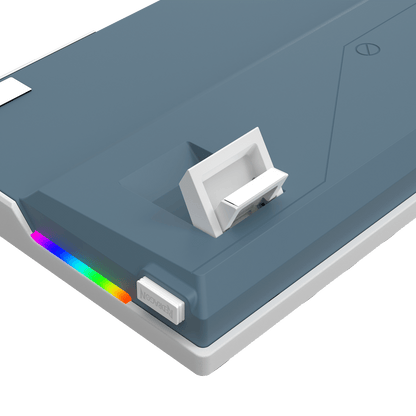 A close-up of a slate blue and white electronic device, likely a power bank or charging hub, featuring a white latch on top, a small white button, and a vibrant RGB rainbow light strip along the edge, shown against a solid black background.