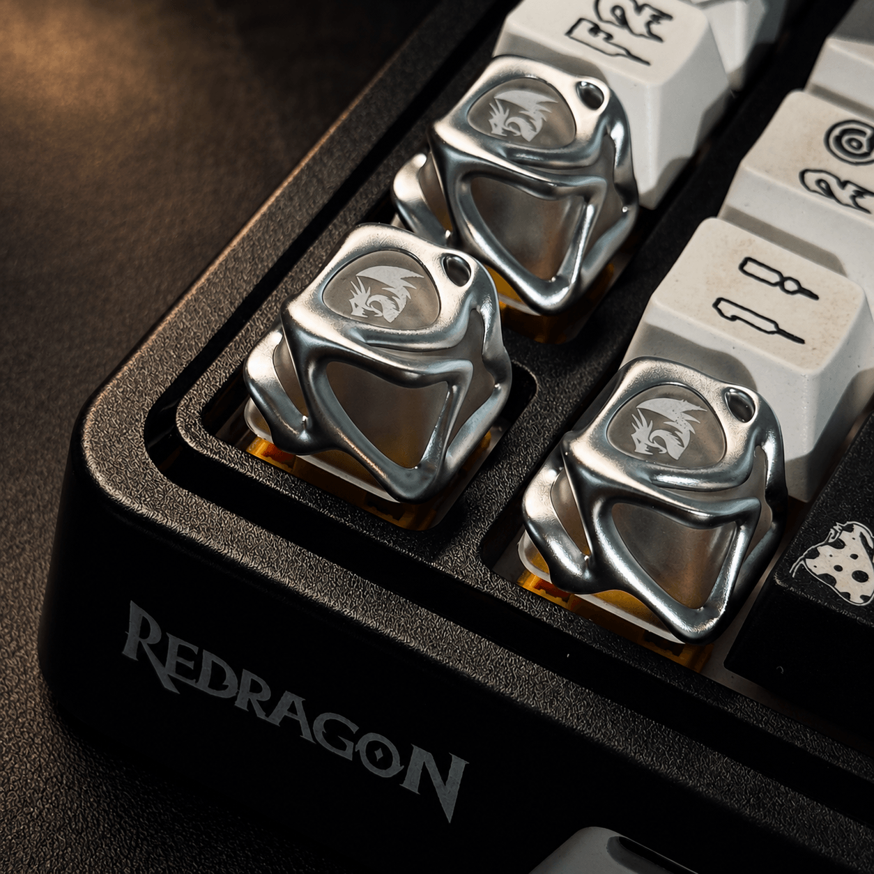 Close-up of a redragon gaming keyboard with metallic keycaps featuring a logo, on a dark surface with 'Redragon' branding.